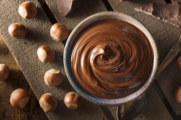 Top view of chocolate spread on a bowl, by the side of hazelnuts